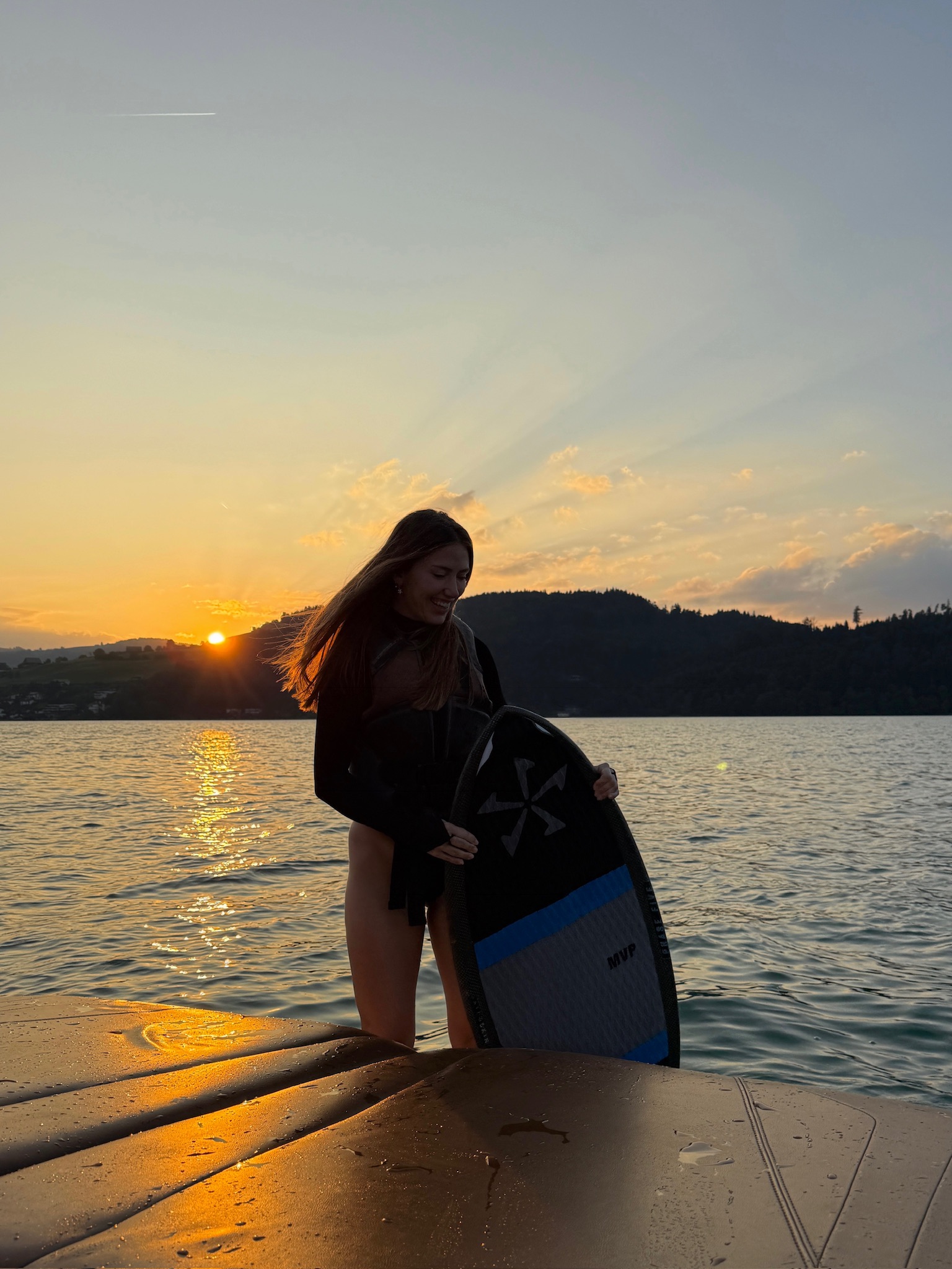 Girl with wakesurf board at sunset on Lake Zug
