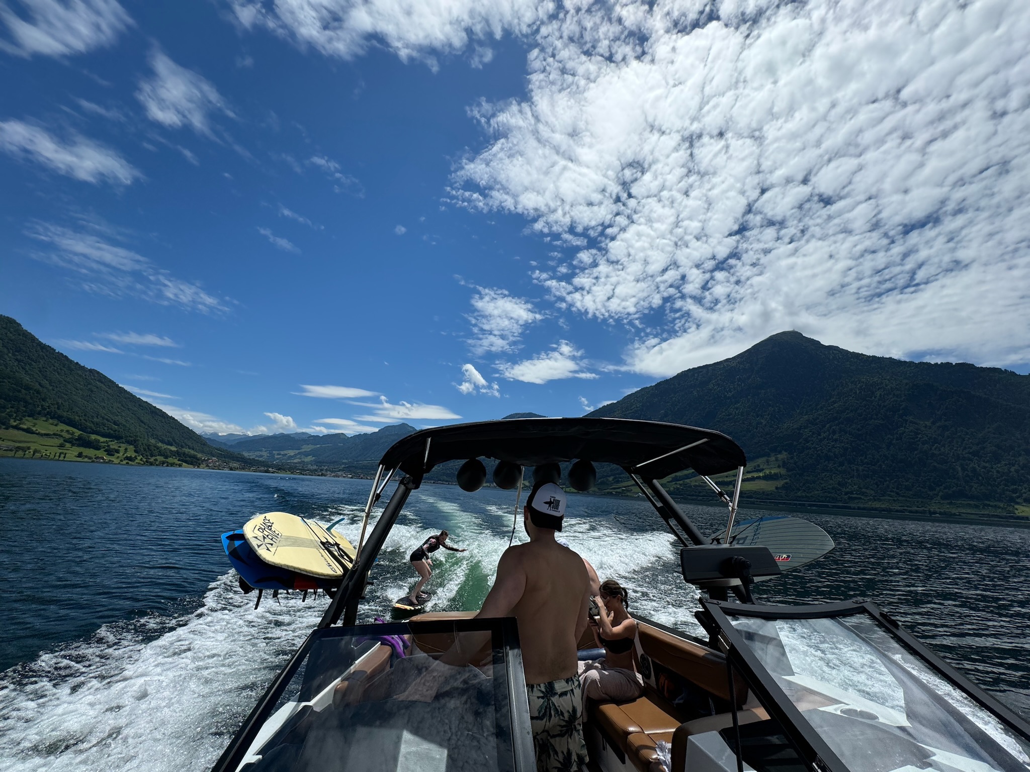 Group on the wakeboat with someone surfing behind on Lake Zug